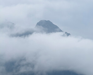 A mountain peak emerges softly through thick clouds, creating a tranquil and mysterious scene