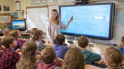 Teacher explains math equations on smartboard to elementary school students - Powered by Adobe