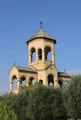 Bell Tower with crosses and Olive Trees at The garden of The Sameba Georgian Orthodox Cathedral with Blue Sky Background in Tbilisi, Georgia