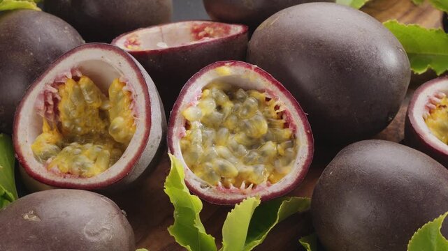Ripe passion fruits with passion fruit seeds and passionfruit leaves slowly move in the frame on a gray stone table. 