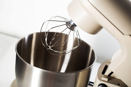 Stand mixer with whisk attachment and empty stainless steel mixing bowl. Kitchen appliance for baking and cooking preparation. - Powered by Adobe