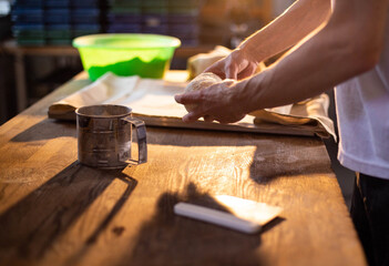 Hands of person shaping dough on wooden table in sunlit kitchen, preparation for baking, traditional craft of bread making, culinary art of fresh baked goods
