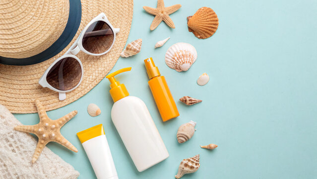 july is uv safety awareness month A straw hat, sunglasses, and sun care products are surrounded by seashells, evoking a beachy vibe.