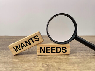 Wants vs Needs concept. WANTS and NEEDS written on wooden blocks with magnifying glass illustrating financial priorities and decision making.