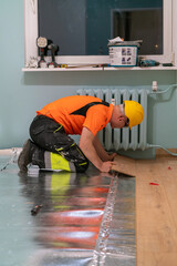 A man is laying wooden flooring. A finishing worker at work. Apartment renovation.