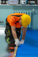 A finishing worker applies an insulating underlayment with an aluminum layer under wooden floor panels. Sound and thermal insulation. Apartment renovation.