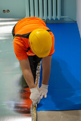 A finishing worker applies an insulating underlayment with an aluminum layer under wooden floor panels. Sound and thermal insulation. Apartment renovation.
