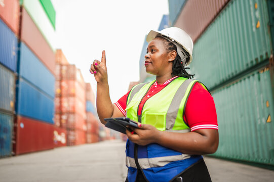 A female logistics worker in safety gear uses a digital tablet, pointing as if interacting with a virtual touchscreen. The scene reflects modern cargo operations and technology-driven supply chain.