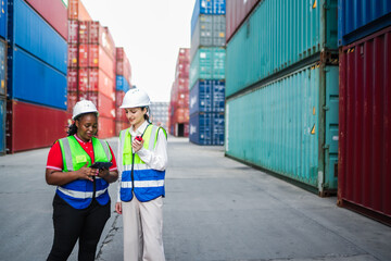 Female engineers in safety vests coordinate cargo tasks, reviewing digital documents and confirming shipment details during a field meeting at a busy container depot.