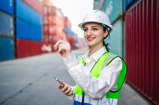 A professional white female worker holding smartphone while pointing at simulated touchscreen in a cargo terminal. Concepts of automation, logistics technology, and digital freight management.