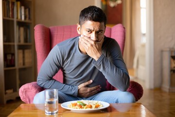 Man sitting in armchair feeling sick and holding his stomach