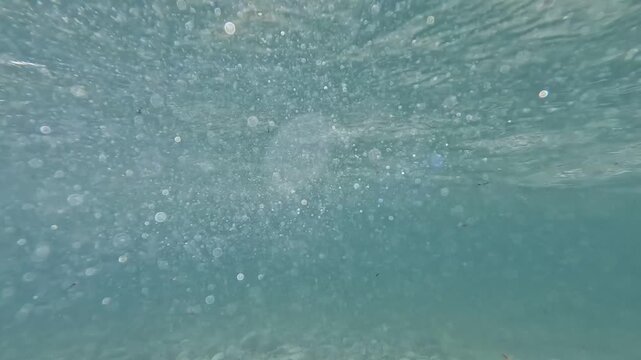 Underwater view of sunlight and tiny air bubbles rising in deep blue sea