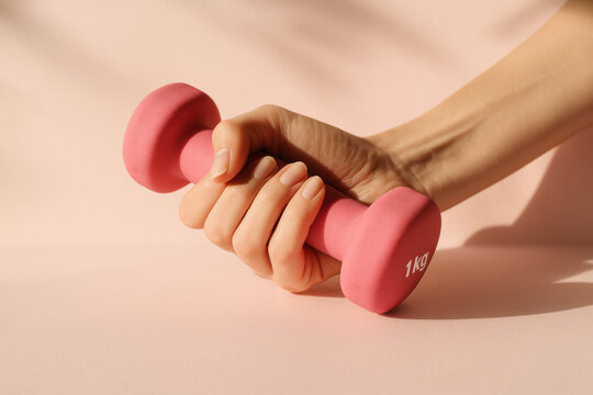 female hand gripping a 1 kg pink dumbbell for light home strength training close up detail conveying fitness wellness dedication and everyday active lifestyle