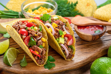 Mexican meat tacos or beef stuffed tortillas and lime slices near them on wooden serving board.