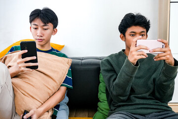 Two Young Friends Enjoy Relaxed Day At Home Together Using Their Smartphone On The Sofa