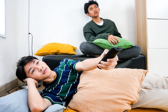 Bored Asian Teenagers Relaxing At Home, One Watching Television With Remote
