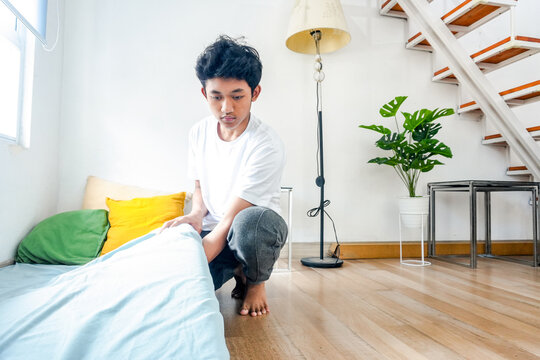 Young Asian male making bed in bright modern bedroom - Powered by Adobe