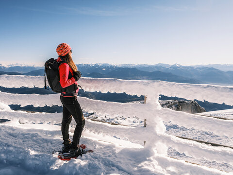 A woman with a backpack gazes at a mountain range from a snow-covered fence. Paganella, Roda refuge,Trentino, Italy