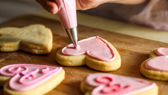 Decorating heart shaped cookies with pink frosting for Valentine's Day celebration baking project