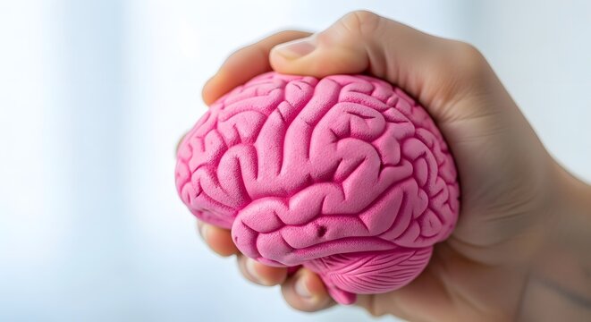 Human hand gently holding a bright pink brain model representing mental health awareness month concept and psychological well-being