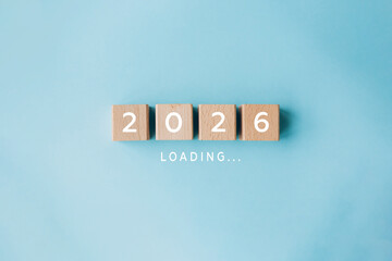 2026 loading concept with wooden cubes on blue background. Concept of new year arrival, anticipation, future plans, and transition from 2025 to 2026.