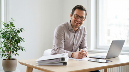 Naklejka premium Smiling Businessman Writing at Desk with Laptop and Plant Background