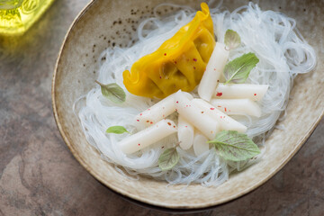Beige bowl with soy bean noodles, tteokbokki or garaetteok and steamed dumpling, horizontal shot, middle close-up, selective focus