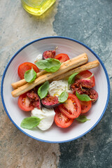 Salad with fresh tomatoes, figs, mozzarella and basil, vertical shot on a grey and beige stone background, elevated view