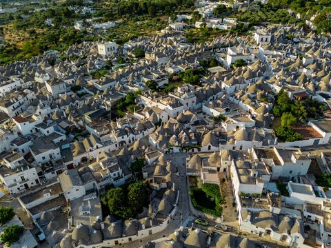 Aerial view of a mesmerizing sea of conical roofs cascading across the landscape, a symphony of white and grey stones under the golden sun, Alberobello, Apulia, Italy.