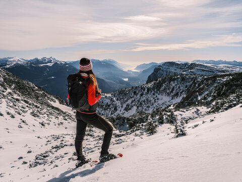 A woman with a backpack and snowshoes gazes at a mountain vista. Paganella, Roda refuge, Trentino, Italy