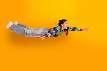 Joyful young woman in striped sweater flies mid air against bright yellow background