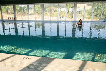 Young woman relaxing in indoor swimming pool with scenic view