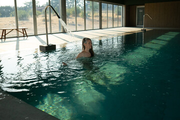 Woman relaxing under waterfall in indoor swimming pool