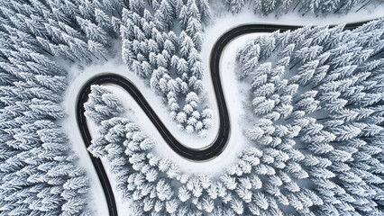 Stunning aerial view of a winding mountain road through snow covered pine trees perfect for travel ads and winter adventure campaigns