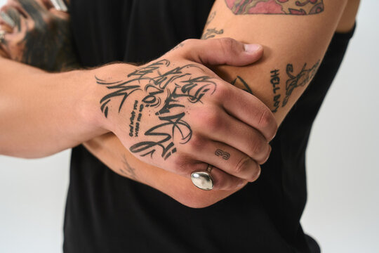 Handsome young man stands confidently, displaying intricate tattoos and stylish attire.