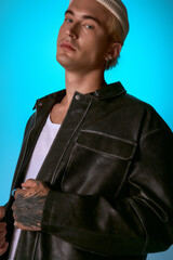 Handsome young man poses with a stylish jacket and cool demeanor against a bright blue backdrop.