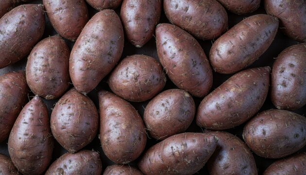 Many whole raw unwashed sweet potatoes with reddish-brown skin are piled together in a full frame top-down view, creating a natural food background
