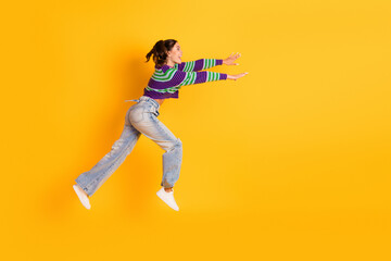 Obraz premium Joyful young woman in striped sweater leaps across a bright yellow background showcasing fashion lifestyle and energetic mood for stock photography