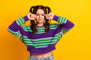 Young woman in colorful striped sweater rubs her eyes against bright yellow background creating a...