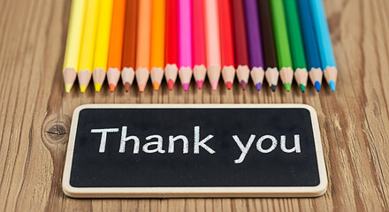 Colorful pencils arranged above a thank you chalkboard on a wooden surface creating a vibrant and grateful scene perfect for educational or appreciation themed projects and designs