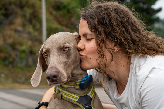 Affectionate Woman Kissing Her Weimaraner Dog on the Head Outdoors