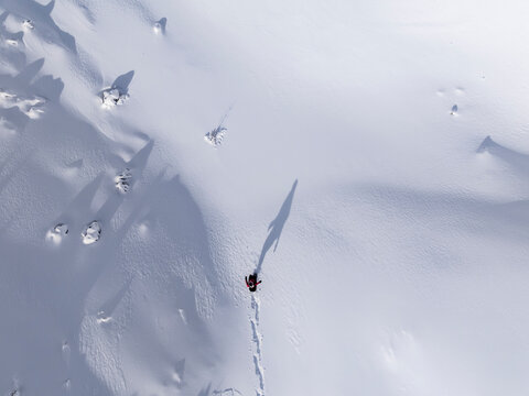 Aerial view of a person hiking in snow, casting a long shadow. Paganella, Roda refuge,Trentino, Italy