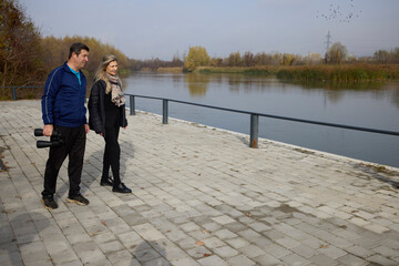Middle-aged woman with a friend on the shore of a water looking for birds through binoculars