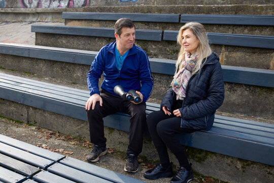 Middle-aged woman with a friend on the shore of a water looking for birds through binoculars