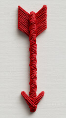 Red arrow crafted from red thread on white textured background, showcasing intricate wrapping and weaving techniques. vibrant color and detailed design create striking visual effect