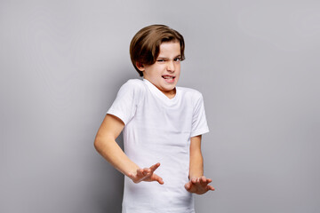 Disgusted young boy reacting with expressive face and defensive hand gesture in studio, emotional response while posing in white t-shirt against grey isolated background for children concepts