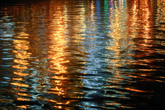 Vibrant multicolored lights reflecting and shimmering on the rippling surface of water creating an abstract and dynamic pattern at night - Powered by Adobe