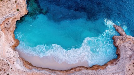 An aerial view of a secluded beach with turquoise water, white waves, and rocky cliffs. The scene is bathed in sunlight.