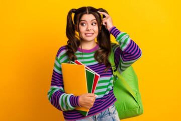 Young student with striped sweater and green backpack holding colorful notebooks against a bright yellow background showcasing fashion style education and cheerful lifestyle