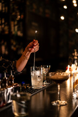 A cocktail being mixed and carefully finished in a bar, presented under warm candlelight.